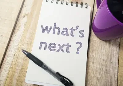 A notebook with "what's next?" written on it, a black pen, and a purple mug rest on the wooden surface, perhaps jotting down plans for a vacation rental franchise in vibrant Miami.