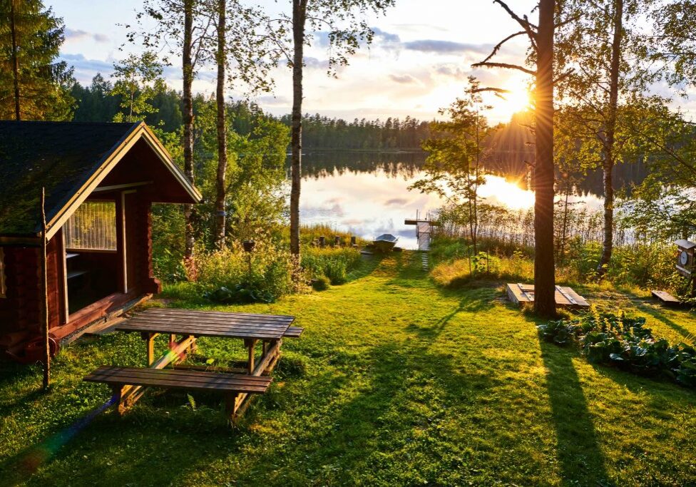 Sunset over a serene lakeside vacation rental business, featuring a small cabin, a boat dock, and a picnic area surrounded by trees and grass.