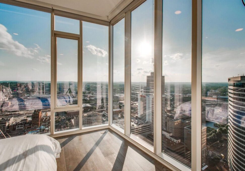 Bright sunlight streaming through corner glass windows in a high-rise building managed by a top-rated property management business, overlooking a cityscape with clear skies.